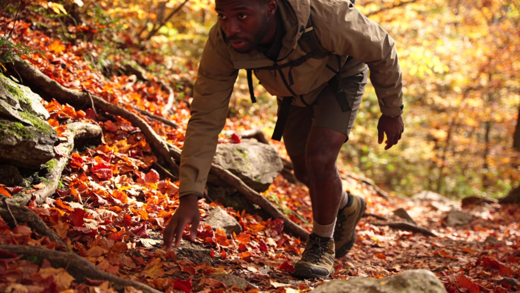 Leaf-covered hiking trail with a hiker walking carefully on wet leaves and uneven terrain during fall