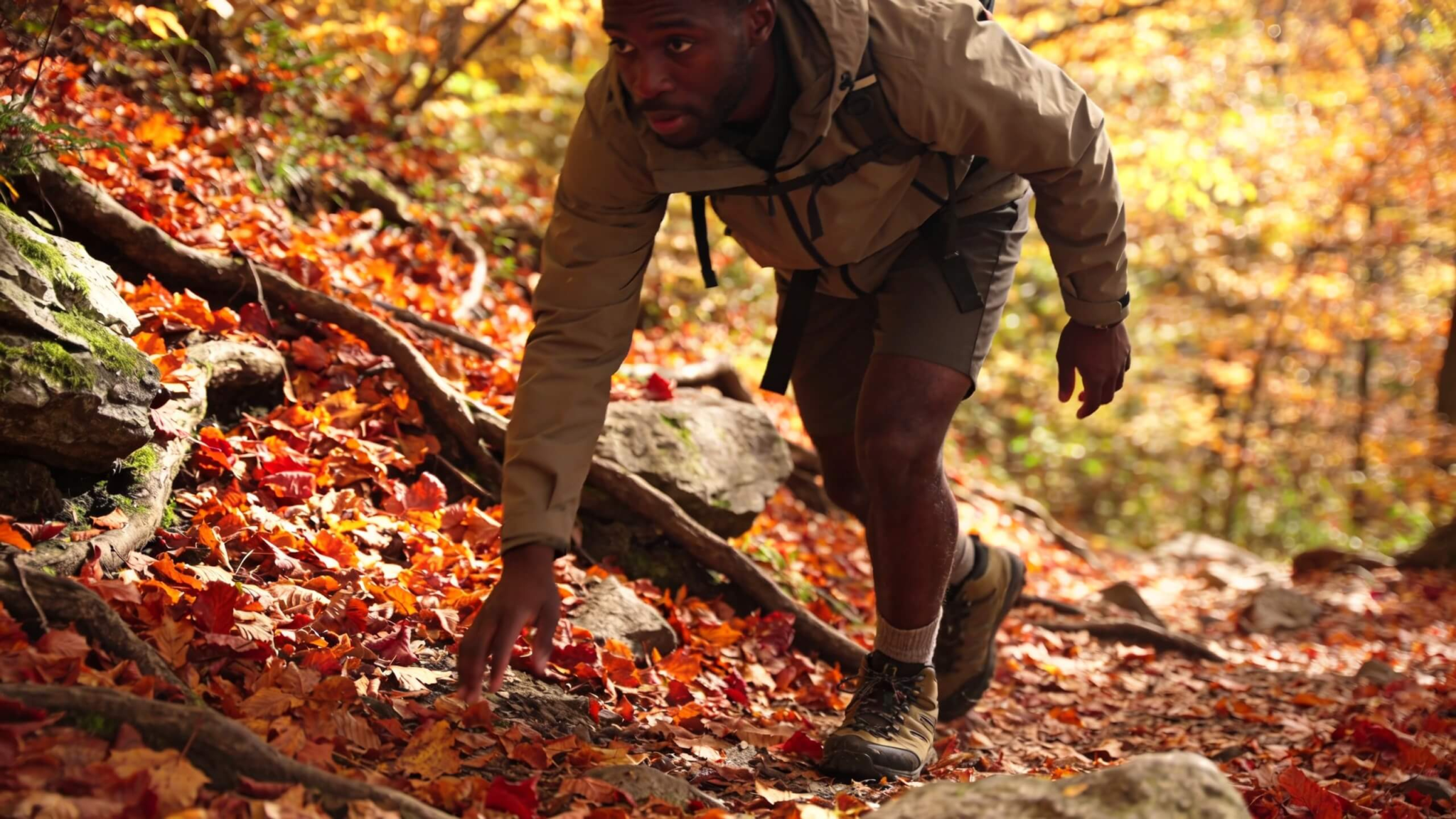 Leaf-covered hiking trail with a hiker walking carefully on wet leaves and uneven terrain during fall