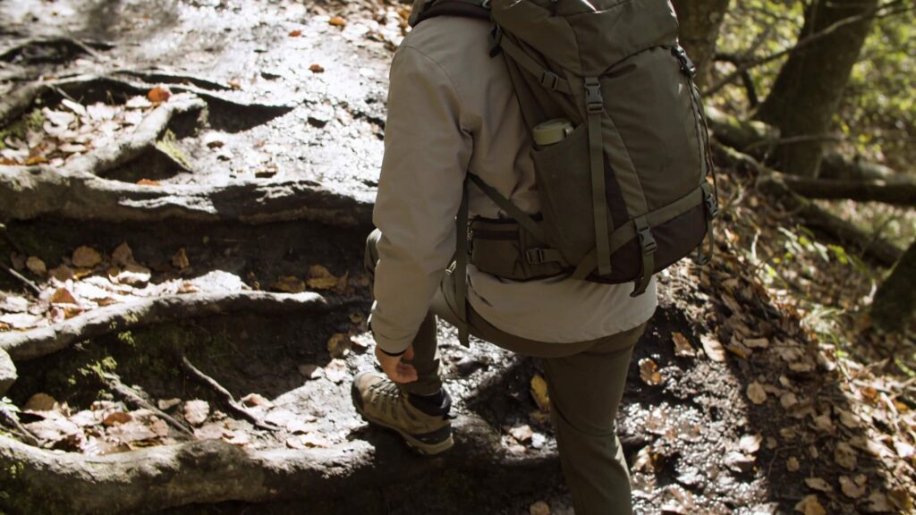 Hiker wearing a properly fitted backpack on a damp leaf-covered trail, showing how fit and weight distribution affect balance.